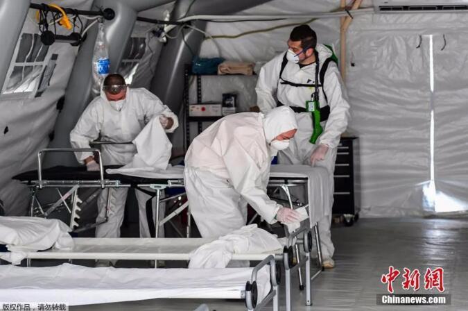 在意大利米兰东南部克雷莫纳，身着防护服的清洁人员正在为收治新冠状肺炎患者的野战医院帐篷内消毒。